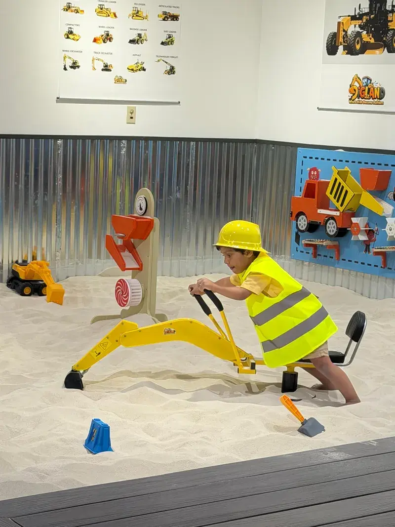 Child in hi-vis working the crane arm in the sand