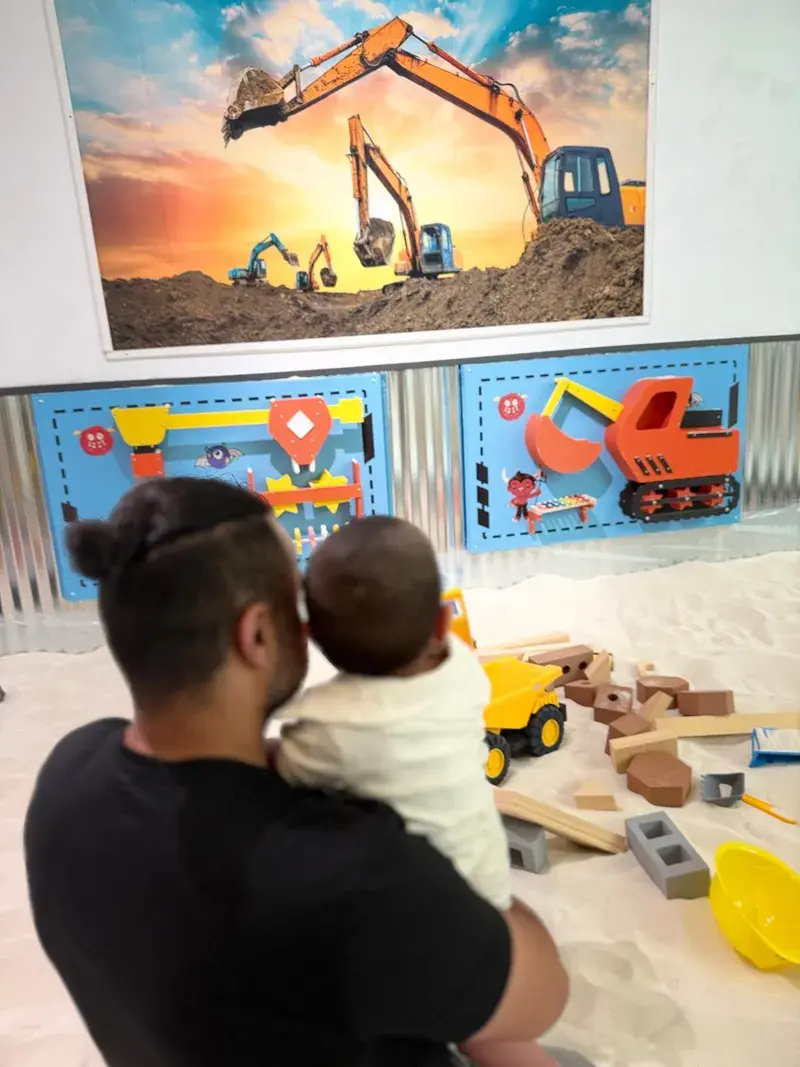 A parent holding a baby at the edge of the sand arena