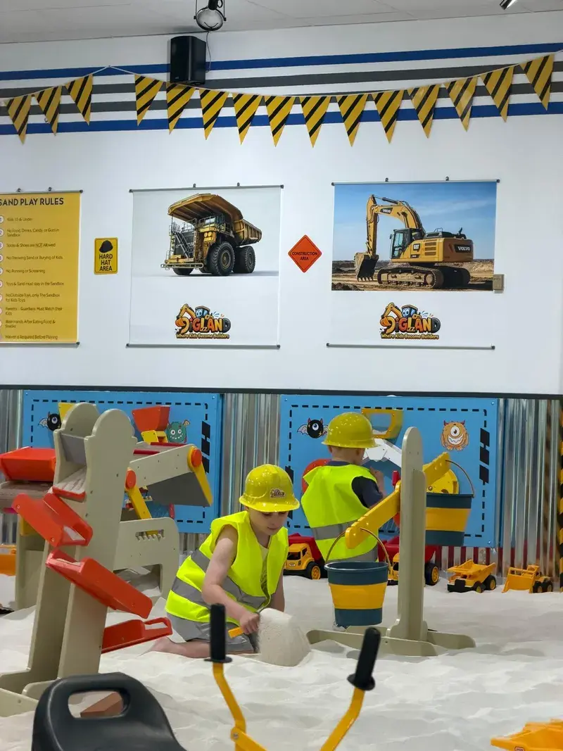 Two children in hard hats and hi-vis vests playing in the sand