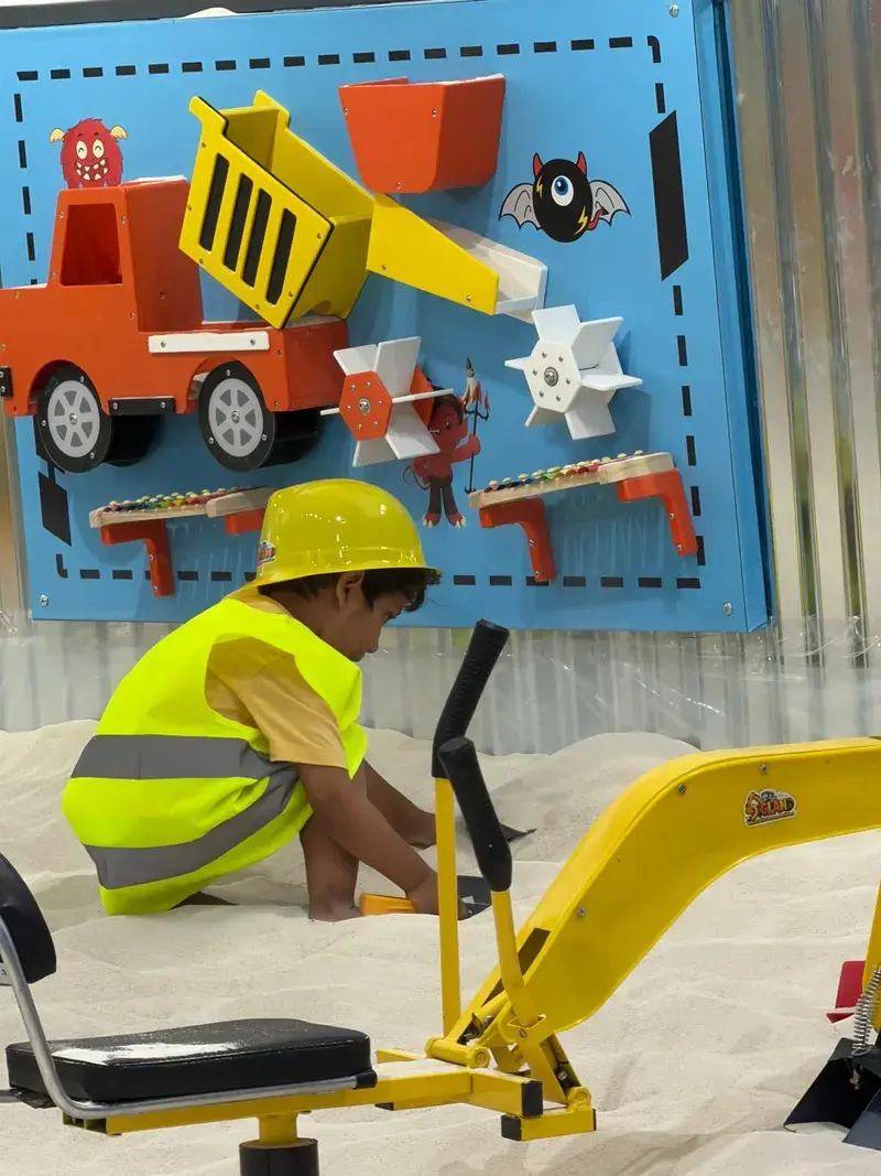 Child in a hi-vis vest and hard hat digging in the sand