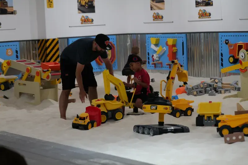 A parent helping a child onto a ride-on digger